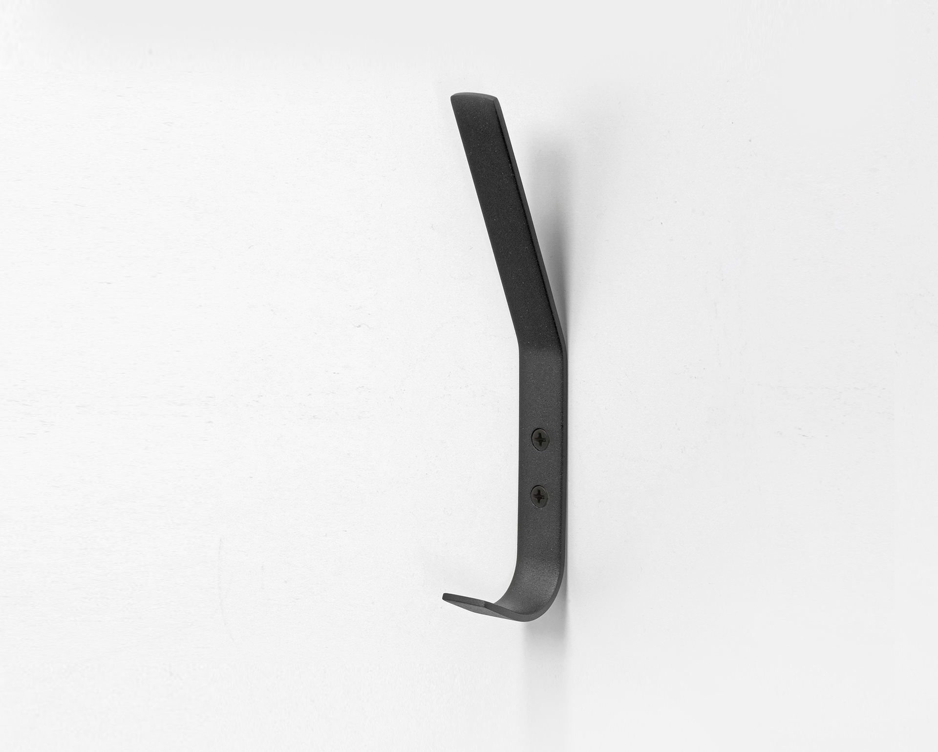 Eurolaton | Ein schwarzer Wandhaken aus Metall wird mit zwei Schrauben an einer weißen Wand befestigt. Der Haken besticht durch ein schlichtes, modernes Design, das von „Möbelgriffe Edelstahl“ inspiriert ist, mit einer nach oben gerichteten Wölbung am oberen Ende und einer kleineren, nach außen gerichteten Wölbung am unteren Ende.
