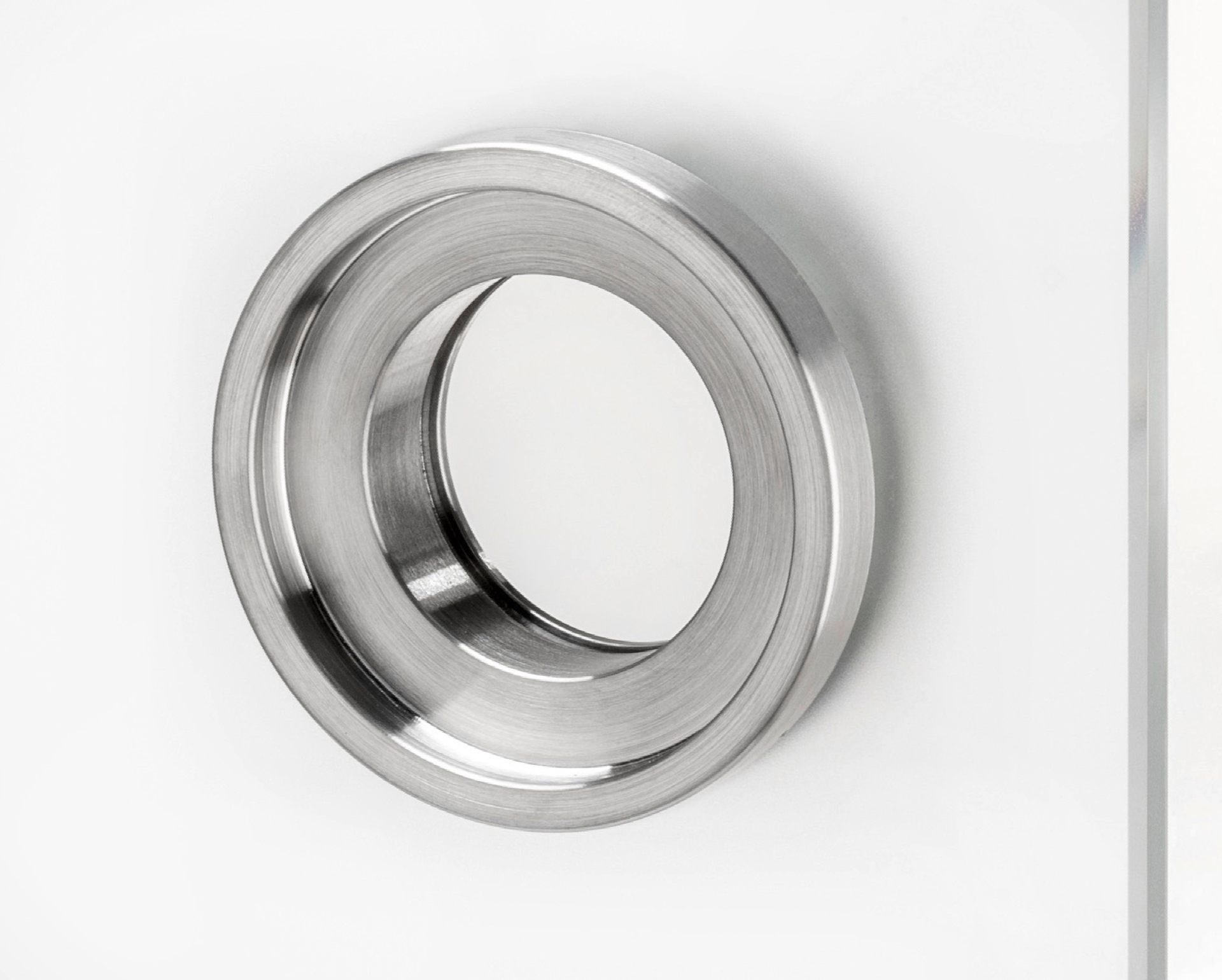 Eurolaton | Eine Nahaufnahme einer runden Metallbeschlagteil oder eines Rings, dessen Oberfläche der eines „Türstopper Edelstahl“ ähnelt, eingebaut in eine klare Glasscheibe – möglicherweise als Griff oder Durchreiche in architektonischen oder industriellen Anwendungen verwendet.