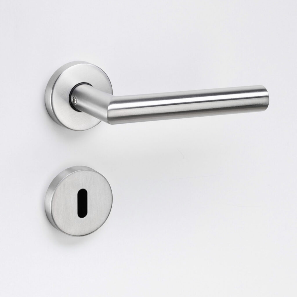 Eurolaton | Eine Nahaufnahme einer modernen Türklinke aus gebürstetem Metall und einer dazu passenden Schlüssellochblende aus unserem Türbeschläge-Sortiment, montiert an einer weißen Tür.